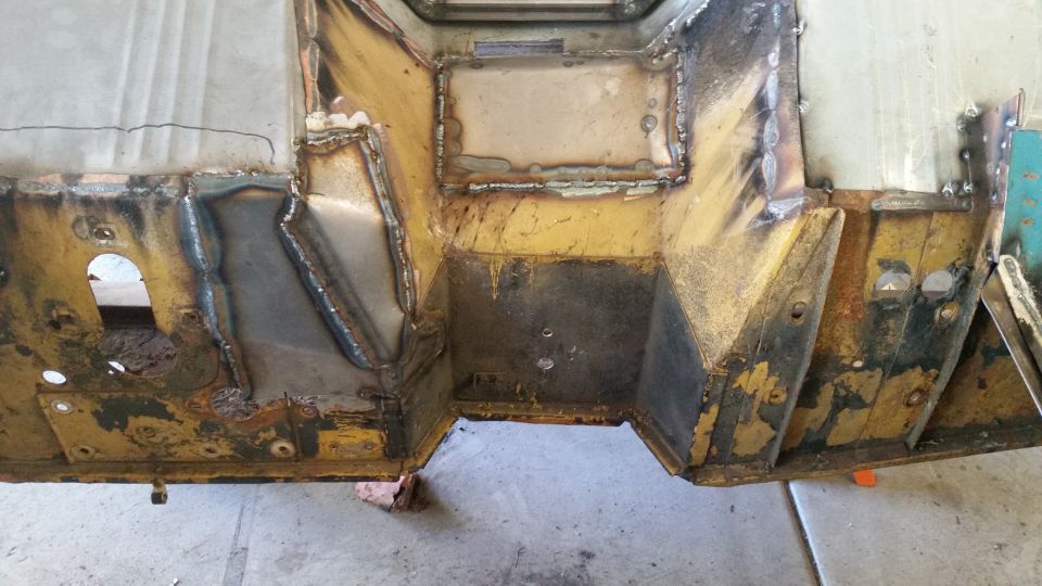 Welded vehicle chassis, floor pan, and firewall with rust and yellow paint.