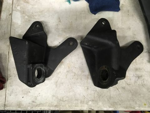 1993 Ford Bronco - Two black metal brackets are shown on a light-colored, textured surface. The bracket on the left has the embossed text "BKB" visible.