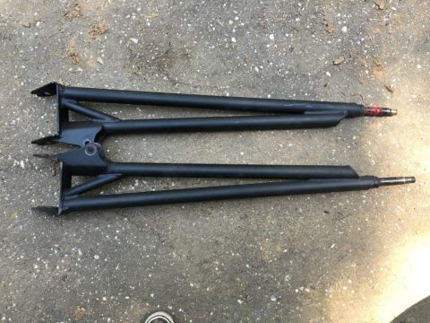 1993 Ford Bronco - Two black, tubular steel control arms with mounting brackets are laid out on a concrete surface. The ends of the control arms have metal sp…