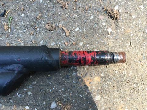1993 Ford Bronco - A close-up view of a black metal part with red paint markings, resting on a gravelly surface. The end of the part shows threads and rust.