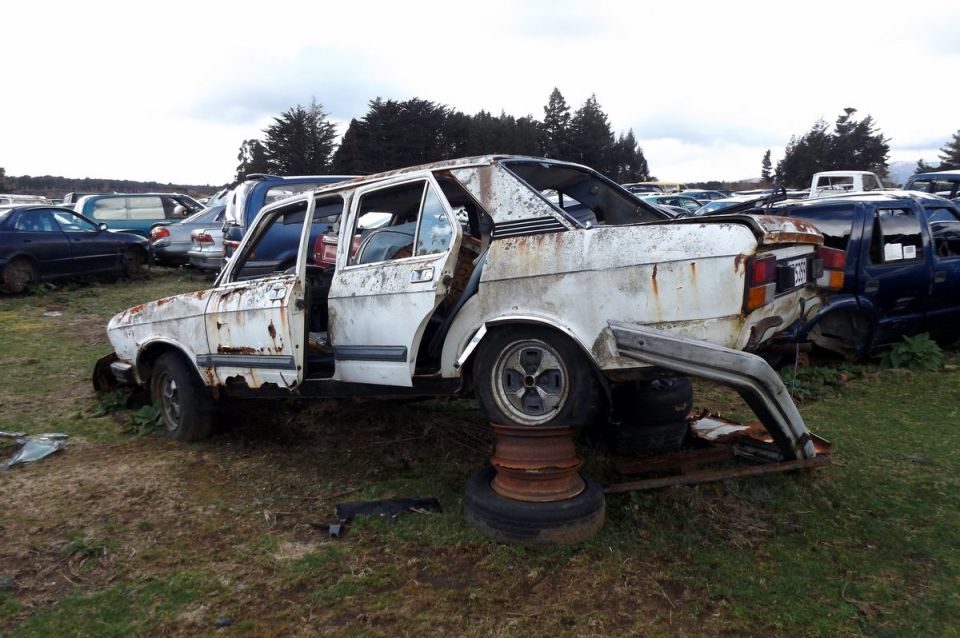Rusted white sedan in junkyard, propped up on tires, doors open.