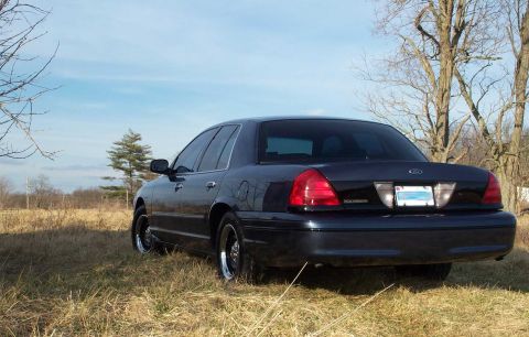 1998 Ford Crown Victoria - Rear view of a 1998 Ford Crown Victoria parked in a grassy field under a clear blue sky.