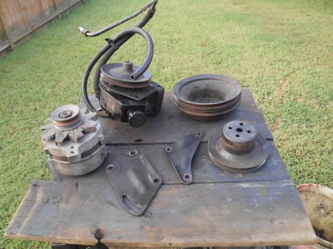 1972 Ford Bronco - A collection of automotive parts, including an alternator, power steering pump with hoses, and several pulleys, are laid out on a wooden ta…