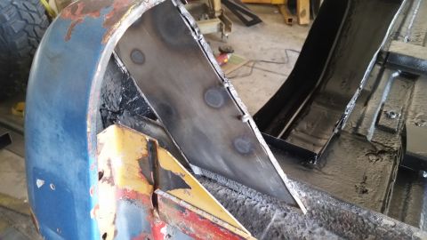 1979 Ford Bronco - Close-up view of the inner wheel well area of a vehicle undergoing restoration. Metal fabrication and welding are visible, along with areas…