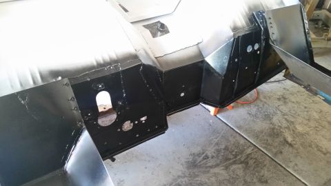 1979 Ford Bronco - The black painted metal chassis of a vehicle is shown from a low angle, with various brackets, panels, and circular cutouts visible. The sc…