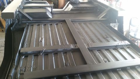 1979 Ford Bronco - The underside of a vehicle, likely a truck or SUV, is shown with a black protective coating applied to the frame and floor pan. Several met…