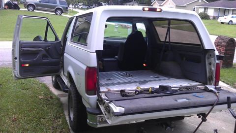 1994 Ford Bronco - The rear passenger side of a white Ford Bronco is shown with the rear tailgate and passenger door open. Tools are visible on the tailgate,…