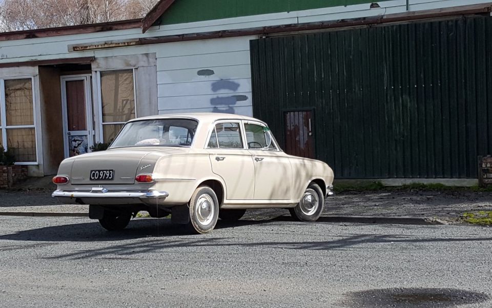 Cream-colored vintage sedan, rear passenger side view, parked in front of a building with a green door.