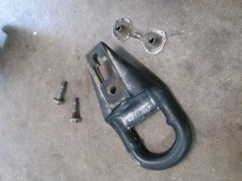 1996 Ford Bronco - A black tow hook assembly with two bolts and a metal bracket are laid out on a concrete surface. The tow hook has the text "WB 7.9005" stam…