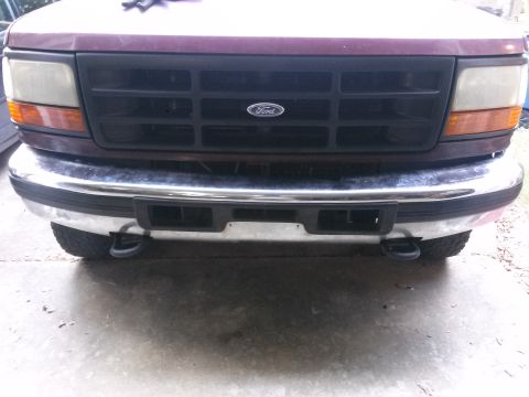 1996 Ford Bronco - Front view of a maroon Ford Bronco with a chrome bumper and black grille. Tow hooks are visible on either side of the front bumper.