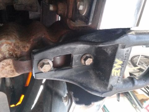1996 Ford Bronco - A close-up view shows a black metal bracket attached to a rusty exhaust pipe with two bolts. Yellow lettering is visible on the bracket, an…