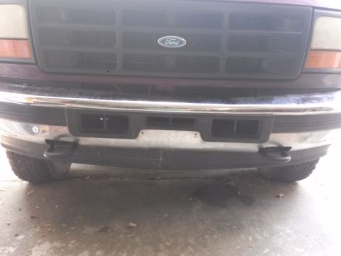 1996 Ford Bronco - Front view of a dark red Ford Bronco's grille and chrome bumper. The vehicle has a black tow hook visible on the driver's side.