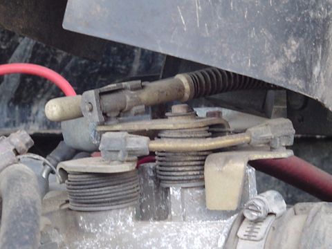 1993 Ford Bronco - Close-up of a throttle body linkage with a red hose and black bellows, showing mechanical components.