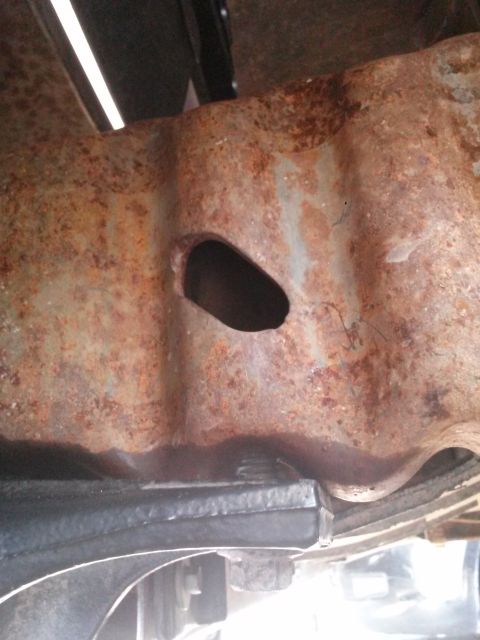 1996 Ford Bronco - A close-up view shows significant rust and a hole in the frame of a vehicle. Below the rusted frame, a black component and suspension parts…