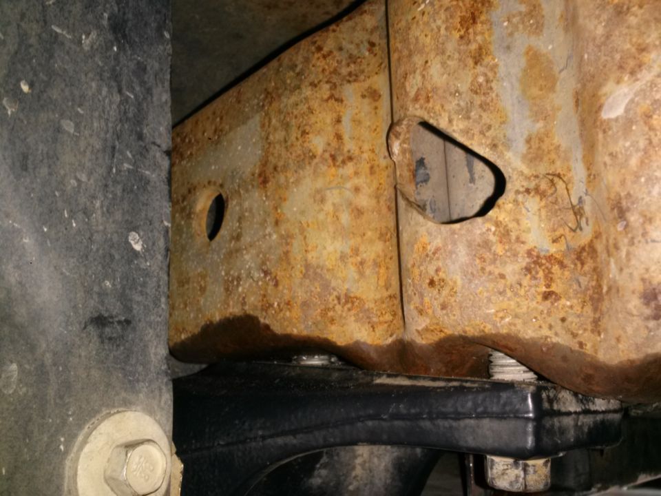 Rusted vehicle frame with a black rubber part and bolt underneath.