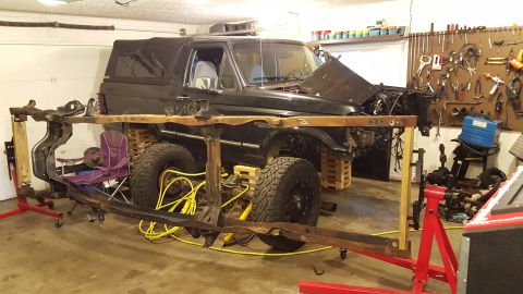 1994 Ford Bronco - A black Ford Bronco is in a garage with its hood open, undergoing restoration. The vehicle's frame is separated from the body and supported…