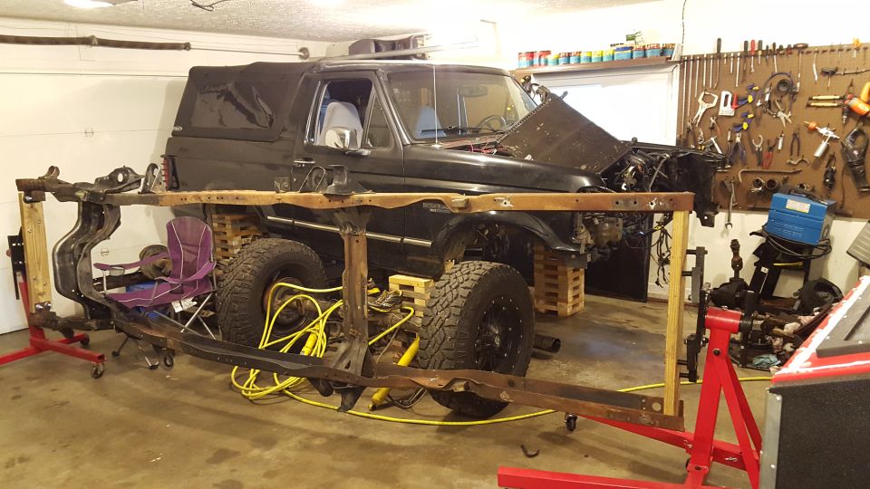 Black Ford Bronco in garage, frame separated from body, hood open, undergoing restoration.