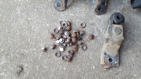 1994 Ford Bronco - A pile of rusty metal washers and bolts are scattered on a concrete surface, with a metal bracket and rubber bushing visible in the upper r…