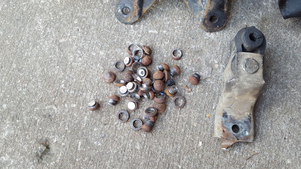Pile of rusty washers and bolts on concrete with metal bracket and bushing.