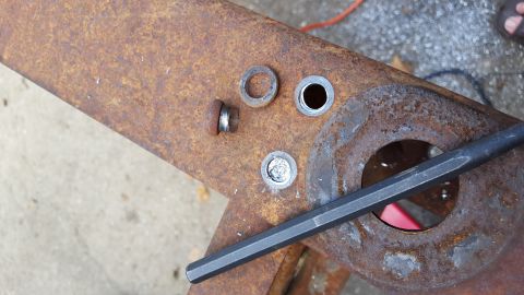 1994 Ford Bronco - A close-up view shows rusty metal components, including bolts, washers, and a hole, with a dark-colored tool resting on the surface. The sc…