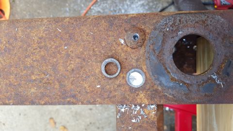 1994 Ford Bronco - A close-up view of a rusty metal frame with two washers and a drilled hole. The frame appears to be part of a vehicle's chassis, possibly f…