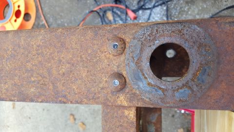 1994 Ford Bronco - Two bolts are visible on a rusty metal frame, with a circular mounting plate to the right. The frame appears to be part of a vehicle's unde…