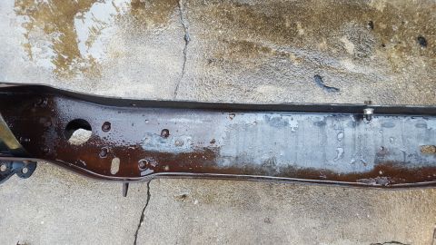1994 Ford Bronco - A close-up, overhead view of a dark, wet metal vehicle frame or chassis component resting on a concrete surface. The part appears to be hea…
