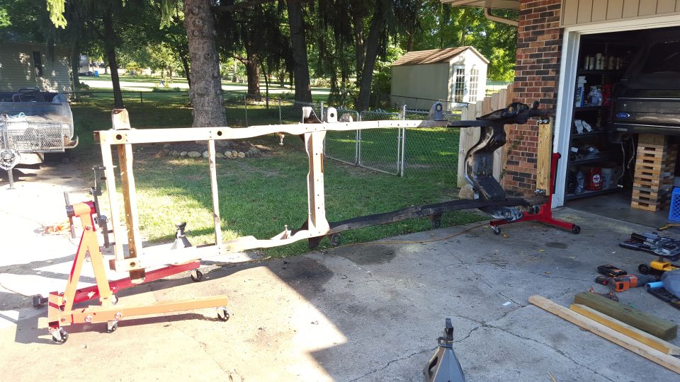 Disassembled vehicle frame on engine hoist and jack stands, driveway, garage, tools
