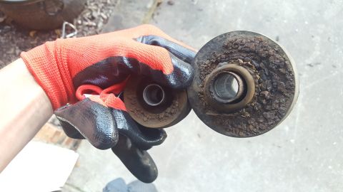 1994 Ford Bronco - A gloved hand holds two worn and corroded metal bushings, likely removed from a vehicle's suspension system. The bushing on the right shows…