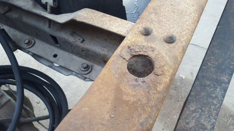 1994 Ford Bronco - The image shows a close-up view of a heavily rusted metal frame, likely from a vehicle's chassis. A large circular hole is visible in the c…