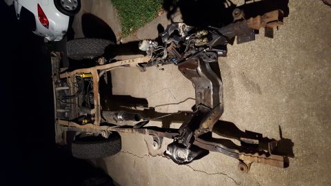 1994 Ford Bronco - The frame and drivetrain of a vehicle are laid out on a concrete surface. Visible components include the engine, suspension parts, exhaust…