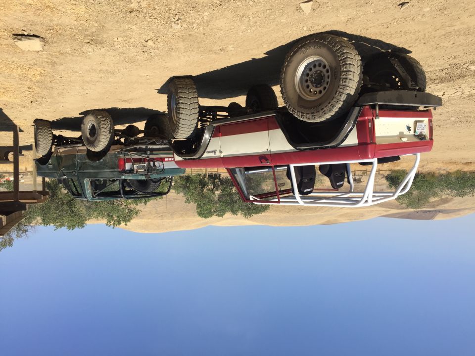 Red-and-white early Bronco and a green Ford pickup parked on dirt terrain