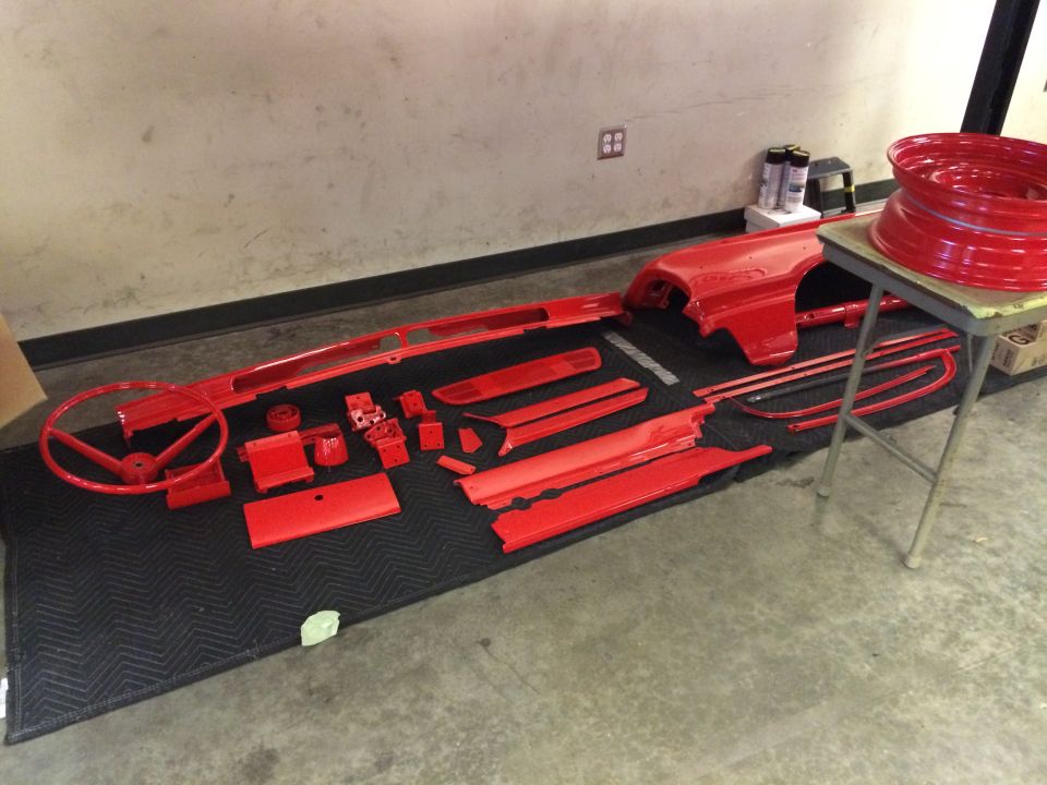 Red painted car parts including steering wheel, fender, trim, and wheel rim.