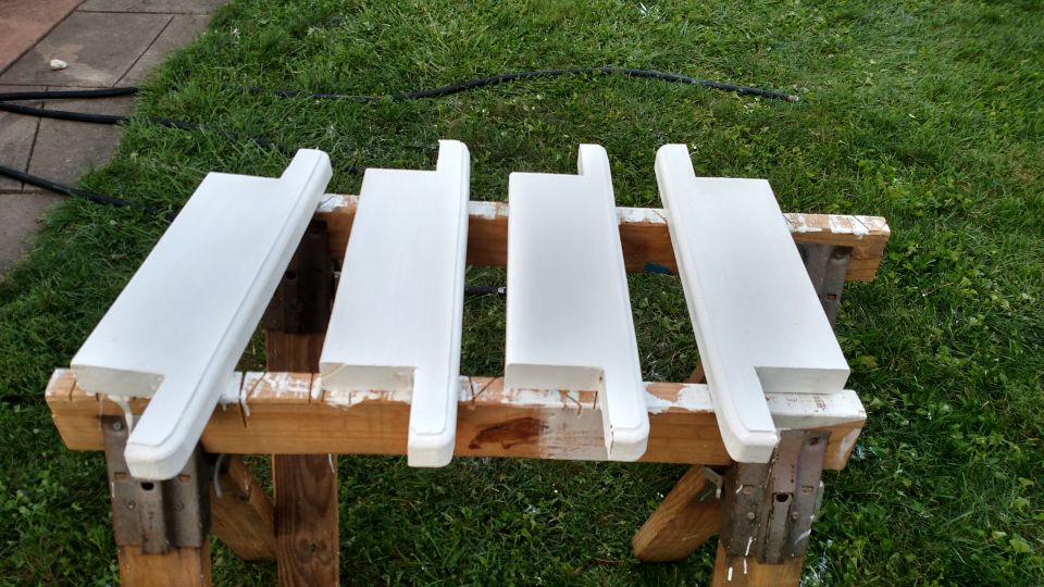 Four white-primed wood shelves drying on sawhorses outdoors