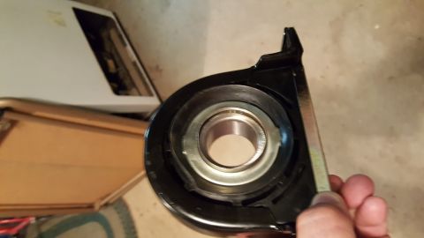 1973 Ford F-100 - A close-up view of a black bearing support bracket with a silver bearing inside. A hand is holding the bracket, with a portion of a white a…