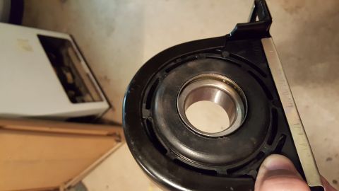 1973 Ford F-100 - A close-up shot shows a black rubber and metal bearing assembly, likely a driveshaft center support bearing. The bearing is held in a black…