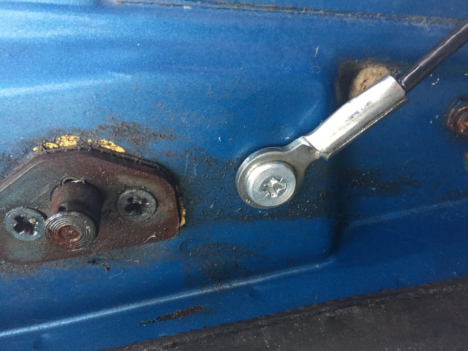 Close-up of a blue vehicle door latch mechanism with rusted parts and a cable attachment.