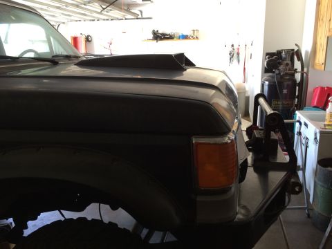 1988 Ford Bronco - The front passenger side of a dark-colored vehicle, possibly a Ford Bronco, is shown in a garage setting. A hood scoop is visible, along wi…