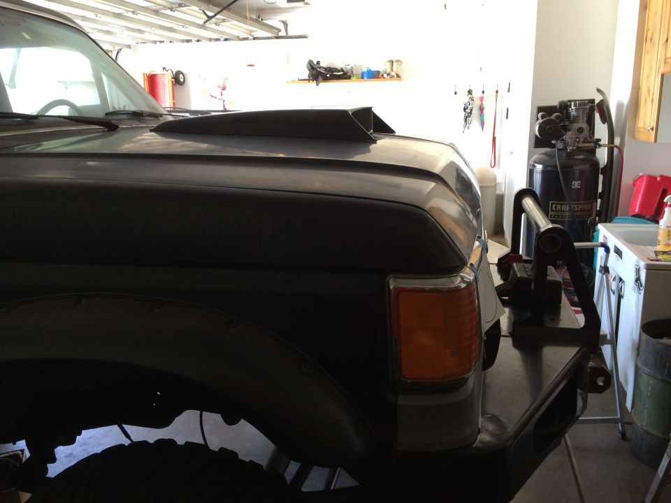 Dark colored vehicle with hood scoop and aftermarket bumper in a garage