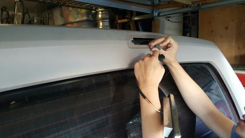1996 Ford Bronco - Two hands connect a two-wire pigtail to a third brake light assembly at the open recess in the white roof panel above an SUV's heated rear…