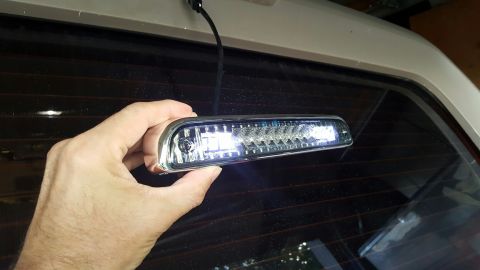 1996 Ford Bronco - A hand holds a new LED third brake light assembly in front of a tinted rear window of a vehicle.