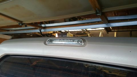 1996 Ford Bronco - The top rear of a light-colored SUV is shown, featuring a third brake light assembly with clear lenses and LED lights. The vehicle is parke…
