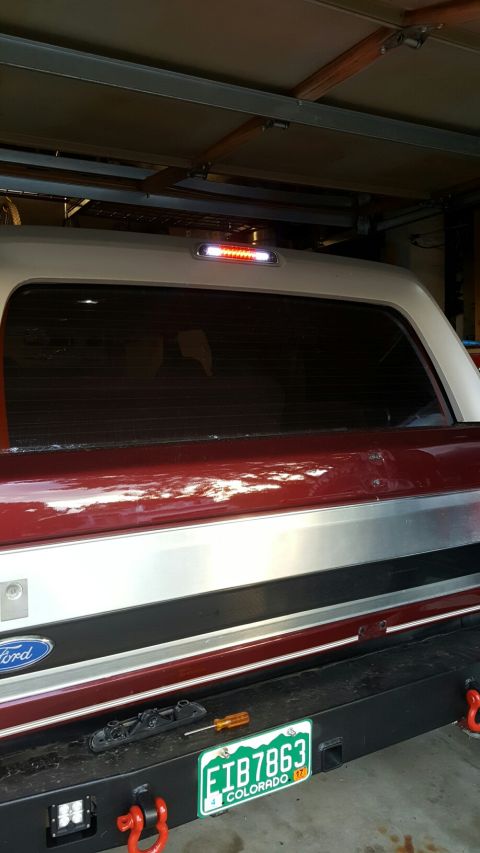 1996 Ford Bronco - The rear of a red and silver Ford Bronco is shown in a garage, with a third brake light illuminated above the rear window. A license plate…