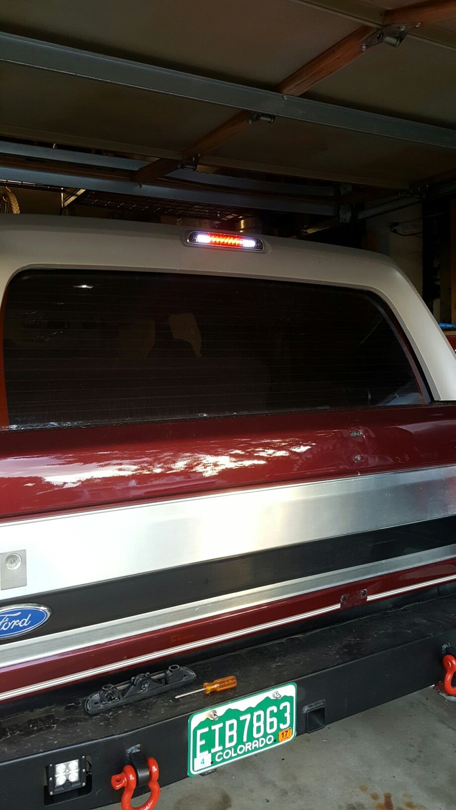 Rear view of a red and silver Ford Bronco with illuminated third brake light and aftermarket bumper.