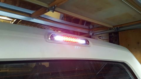 1996 Ford Bronco - Close-up of a clear-lens third brake light illuminated on the white roof panel above the rear glass of an SUV, showing a row of red LEDs pl…