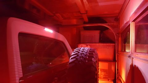 1996 Ford Bronco - The interior of a vehicle is illuminated by red lighting, showing a spare tire mounted on the rear and storage containers.