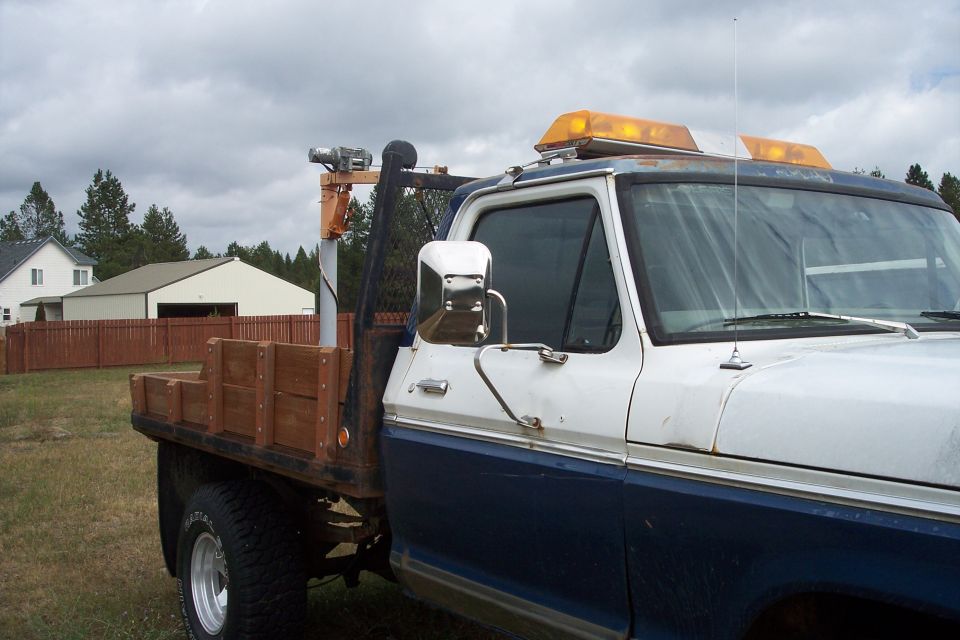 Blue and white Ford F-250 flatbed truck with winch and amber lights.