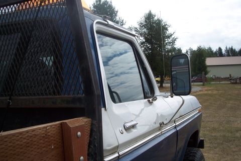 1973 Ford F-250 - Close-up side view of a white and blue pickup truck, showing the driver's side door, window, and side mirror. The truck has a metal mesh ra…
