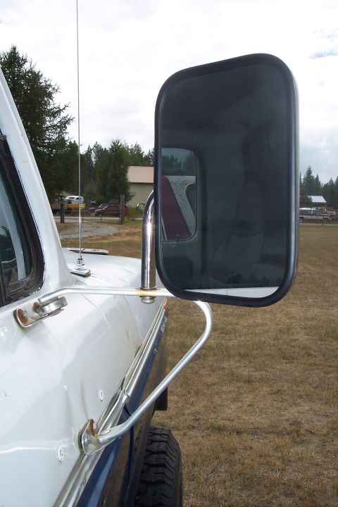 1973 Ford F-250 - A close-up side view of a white and blue truck's exterior mirror assembly and part of the door. The large, dark mirror reflects the interio…