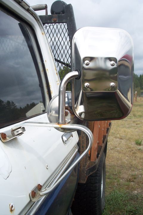 1973 Ford F-250 - A close-up side view of a white pickup truck's side mirror assembly and door. The chrome mirror housing is mounted on a metal arm attached…